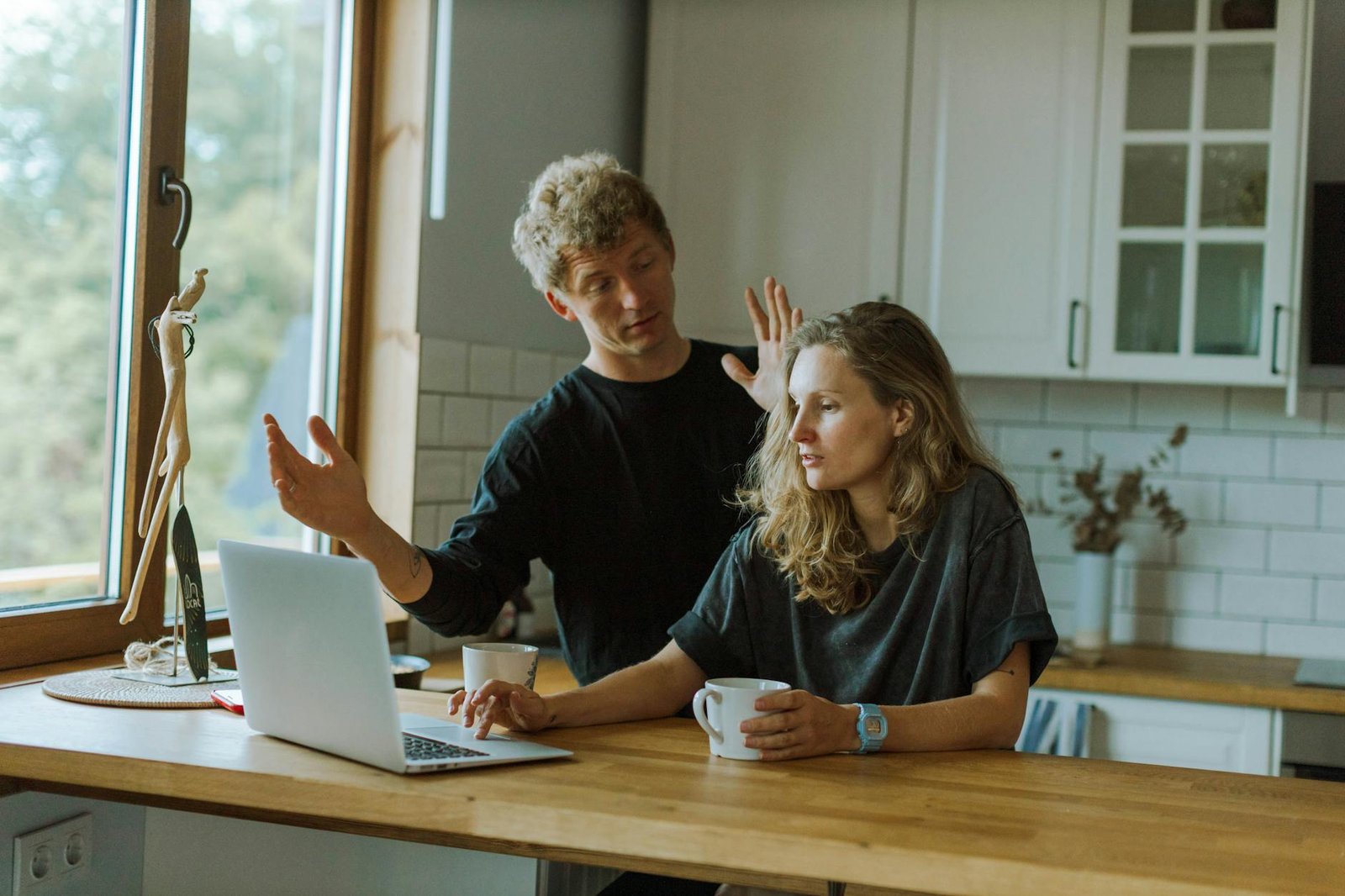 a man beside a woman using a laptop on a wooden counter